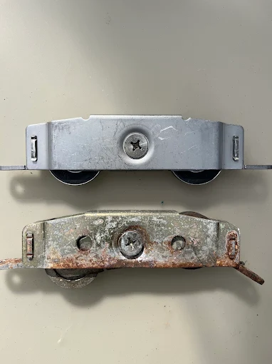 Close-up of a rusted sliding door roller next to a new replacement